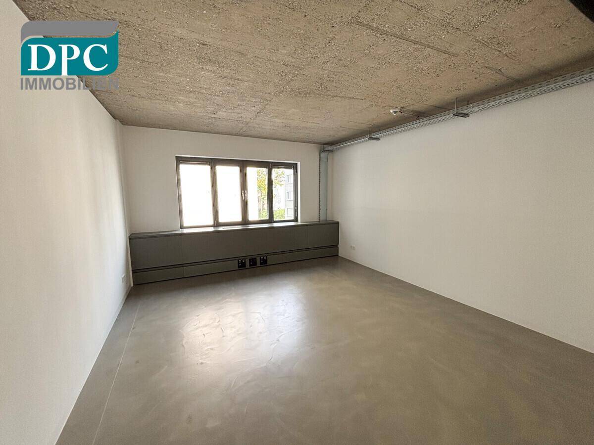 Kleinerer Büroraum mit Sichtbetondecke, Betonboden und einem Fenster für Tageslicht.