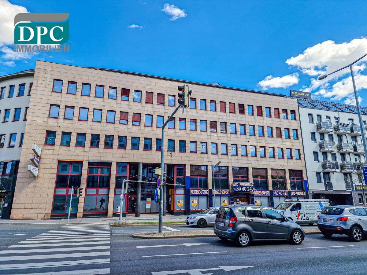 Weitwinkelaufnahme des modernen Bürokomplexes an einer belebten Straße mit weiteren Gebäuden im Hintergrund.