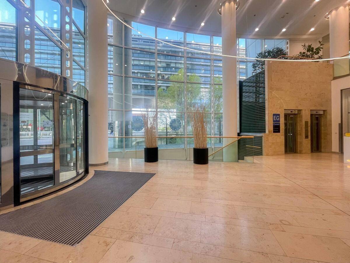Eindrucksvolle, moderne Lobby mit hohen Decken, Marmorboden, Glasfassade und Aufzügen.