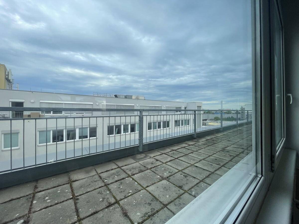 Große Dachterrasse mit Fliesenboden und Metallgeländer, umgeben von anderen Gebäuden.