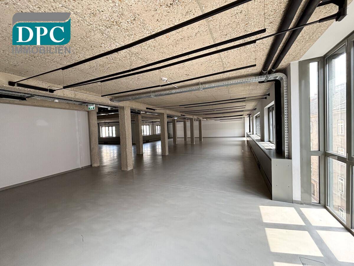 Heller, offener Gewerberaum mit durchgehenden Fensterbändern und sichtbaren Installationen an der Decke.
