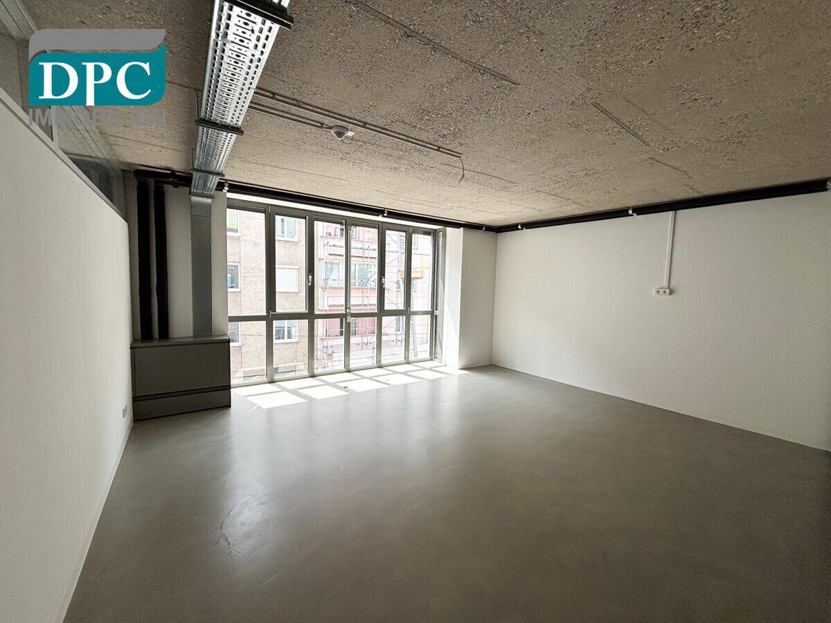 Heller Büroraum mit großem Fenster, Sichtbetondecke und modernem Betonboden.