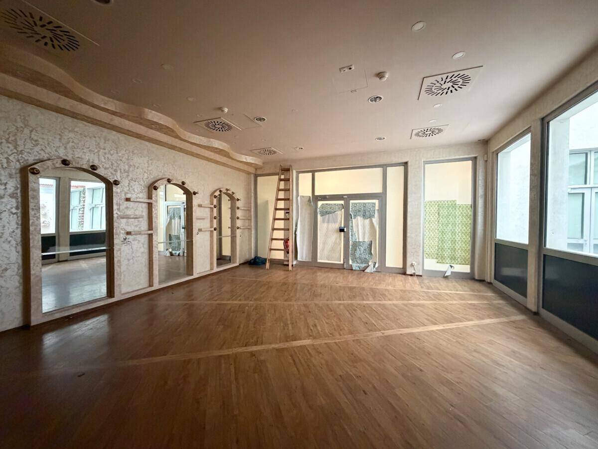 Großer Gewerberaum mit Holzboden, dekorativen Spiegeln und viel Tageslicht durch die Fensterfront.