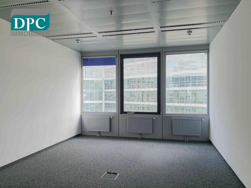 Helles Büro mit Teppichboden, Heizkörpern unter den Fenstern und Jalousien.