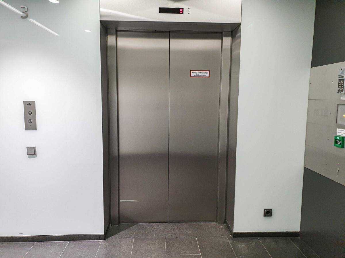 Edelstahl-Aufzugstür mit Bedienfeld in einem modernen Flur.