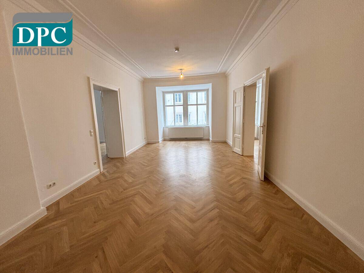 Helles Wohnzimmer mit klassischem Fischgrätparkett, Stuckdecken und hohen Fenstern, ideal für ein stilvolles Zuhause.