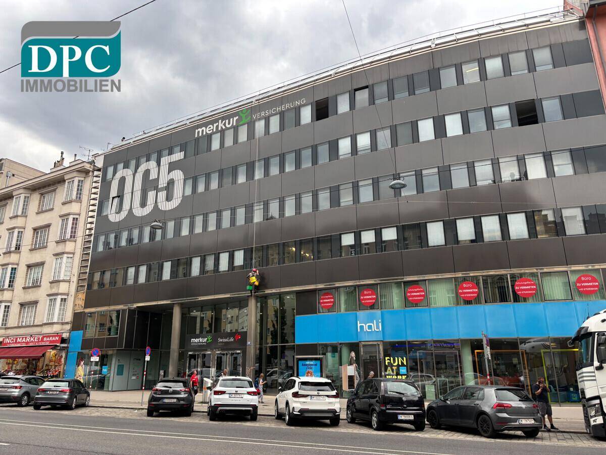 Moderne Geschäftsfassade mit großen Fenstern, Werbeschildern und parkenden Autos davor.