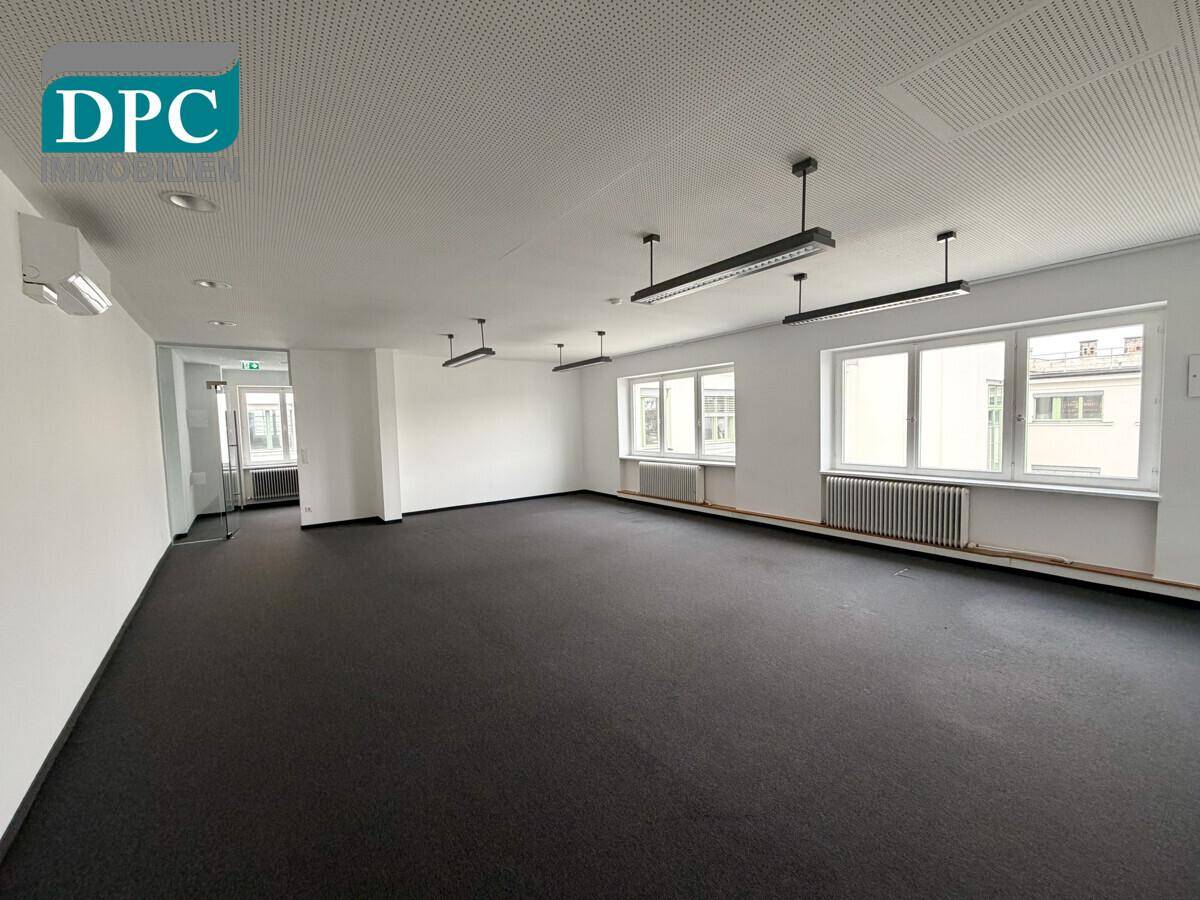 Helles Büro mit Teppichboden, Rasterdecke und mehreren Fenstern für viel Tageslicht und eine angenehme Arbeitsatmosphäre.