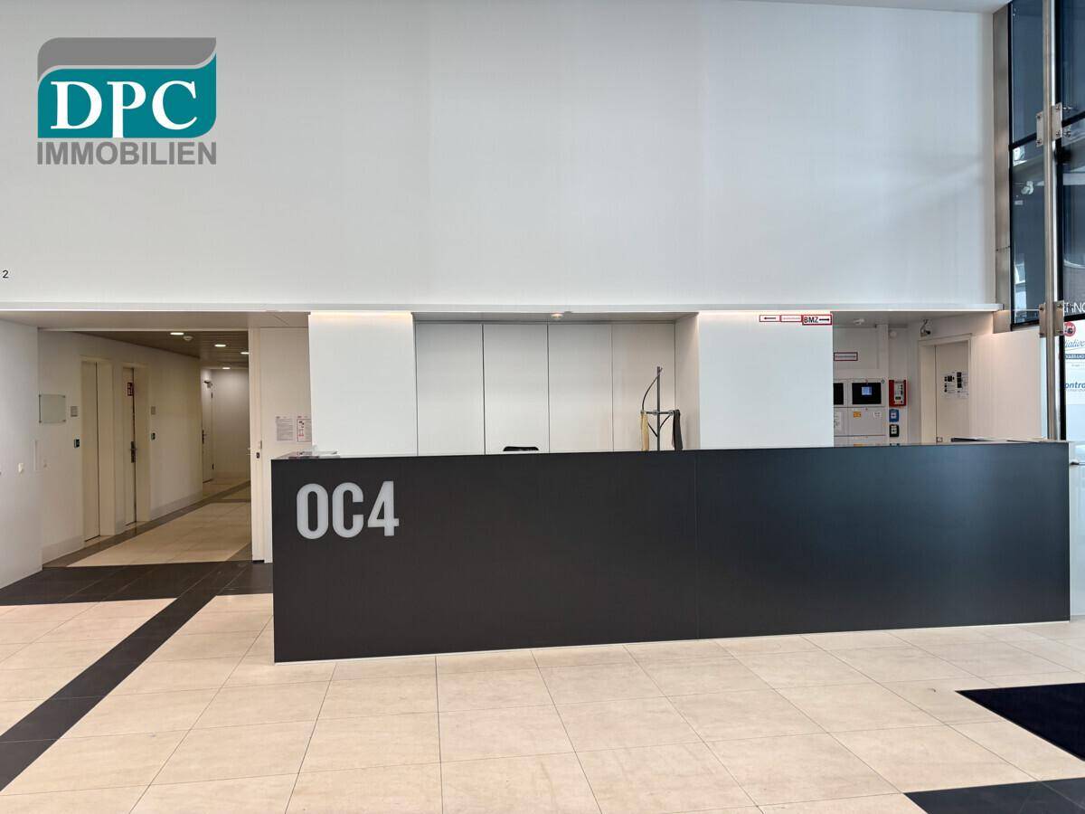 Empfangsbereich mit modernem Schreibtisch und Fliesenboden, Teil einer größeren, hellen Lobby.