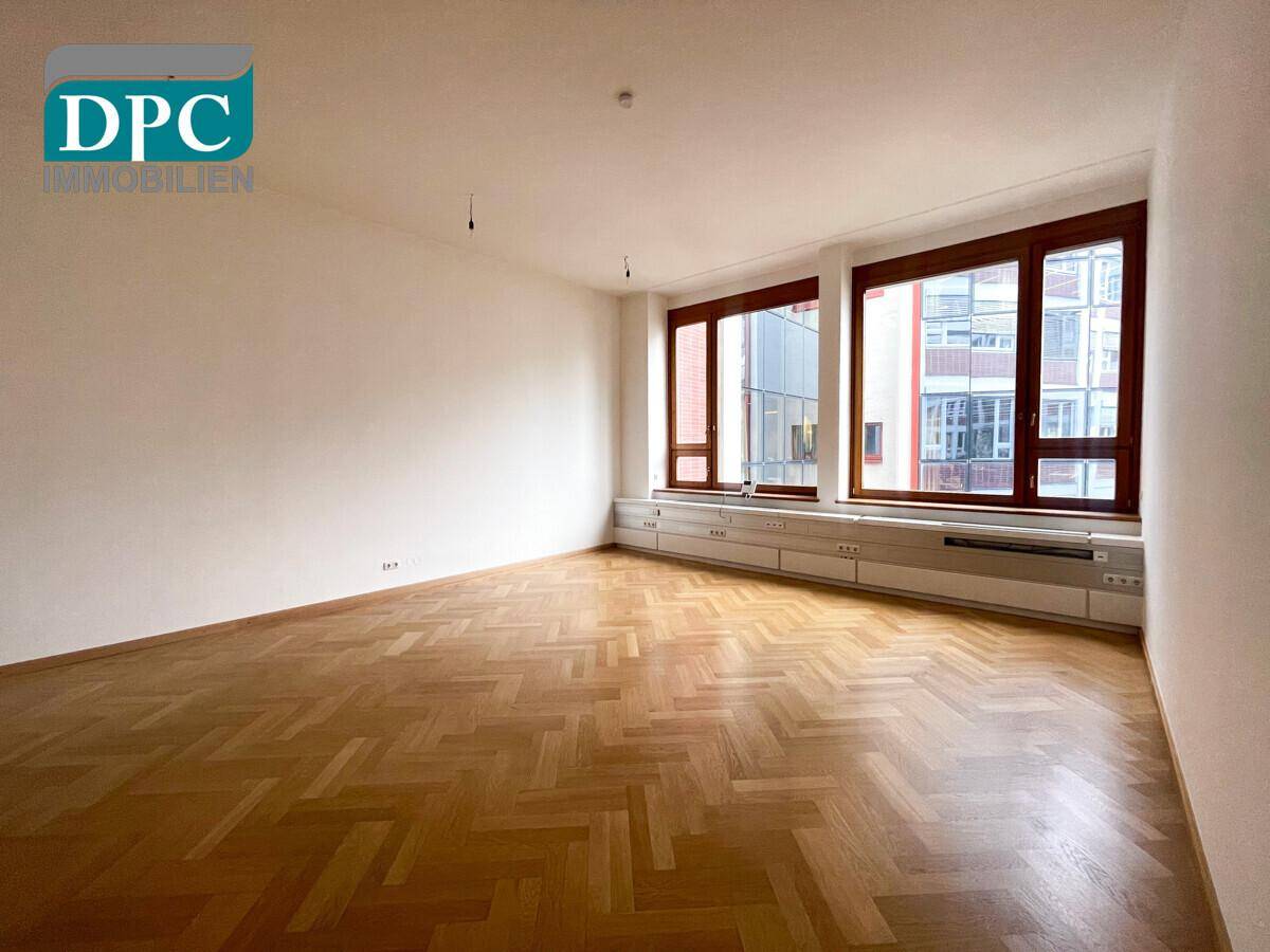 Heller Raum mit großen Fenstern und Fischgrätparkett, ideal für Wohn- oder Büronutzung.
