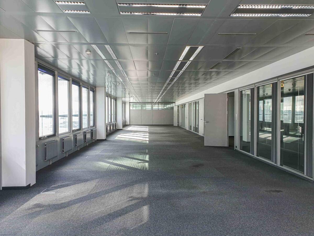 Weitläufiges Büro mit Teppichboden, vielen Fenstern und Glastrennwänden für separate Arbeitsbereiche, hell und modern.