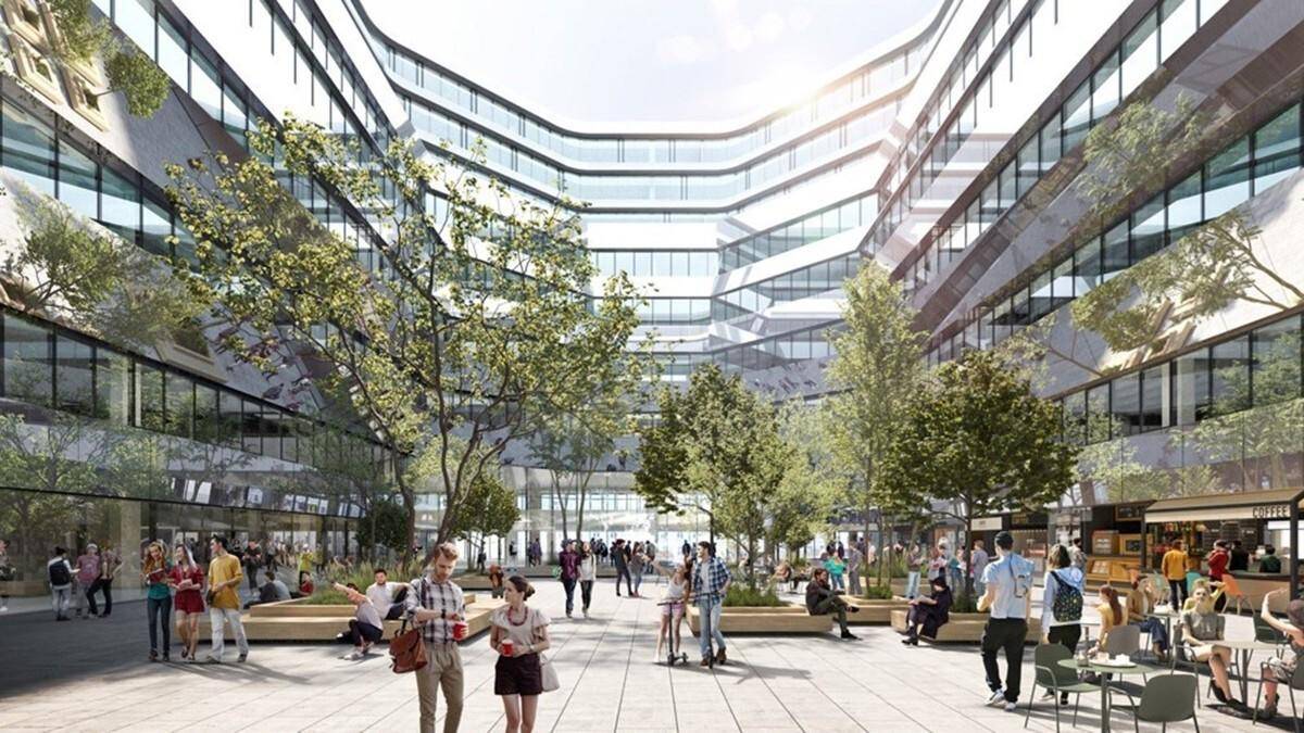 Belebter Innenhof eines modernen Gebäudekomplexes mit Bäumen, Sitzgelegenheiten und Geschäften im Erdgeschoss.