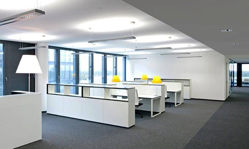 Helles Büro mit mehreren Arbeitsplätzen, modernen Möbeln und Blick auf die Stadt durch große Fensterfronten.