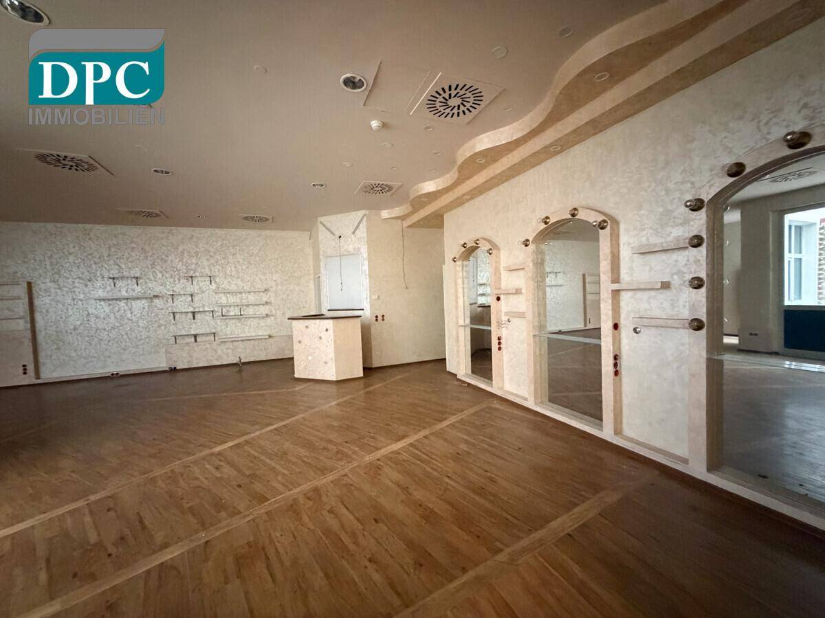 Geräumiger Gewerberaum mit Holzboden, strukturierten Wänden, Spiegeln und einem Holztresen.