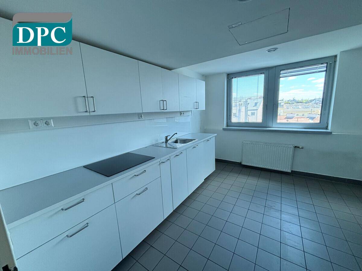 Funktionale Küche mit weißen Schränken, Induktionskochfeld, Spüle und Fliesenboden, ideal für Mitarbeiter.