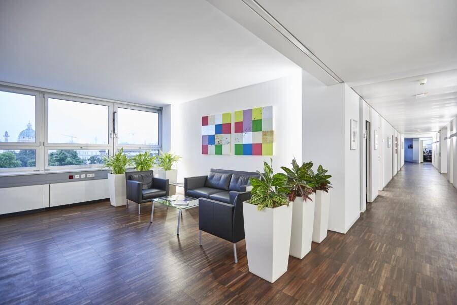 Heller Wartebereich mit großen Fenstern, dunklem Holzboden und modernen Sitzgelegenheiten.