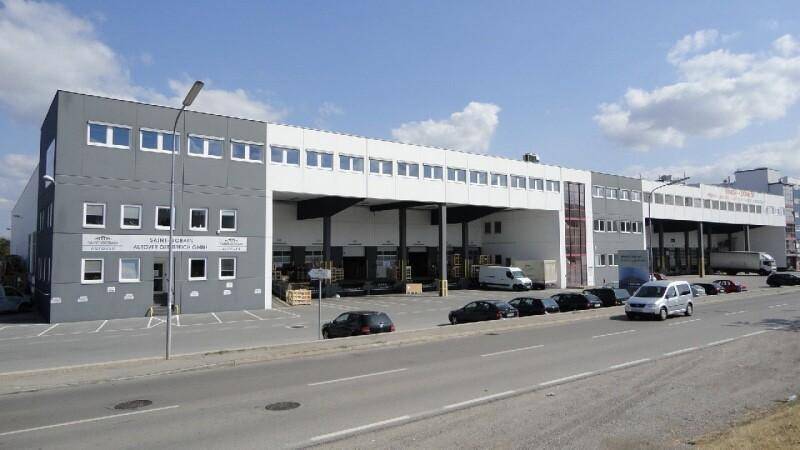 Großes Gewerbegebäude mit grauer und weißer Fassade, mehreren Laderampen und Parkmöglichkeiten.