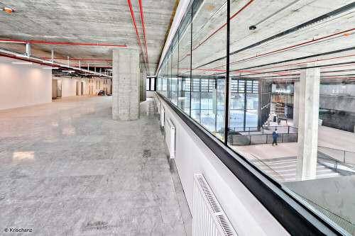 Moderner Korridor im Rohbau mit Betonboden und Glasbrüstung, die den Blick auf eine untere Etage freigibt.
