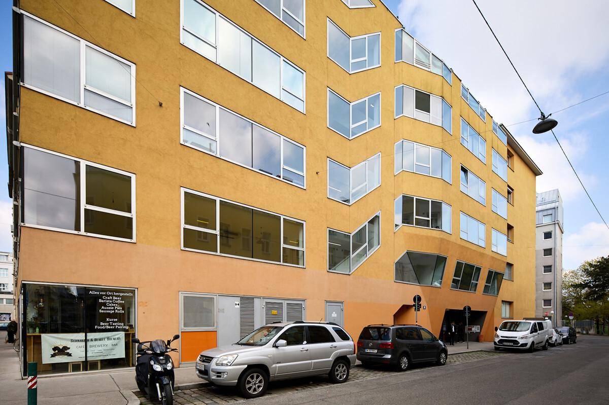 Moderne Fassade eines Gebäudes mit gelben und orangefarbenen Akzenten sowie vielen unregelmäßigen Fenstern.