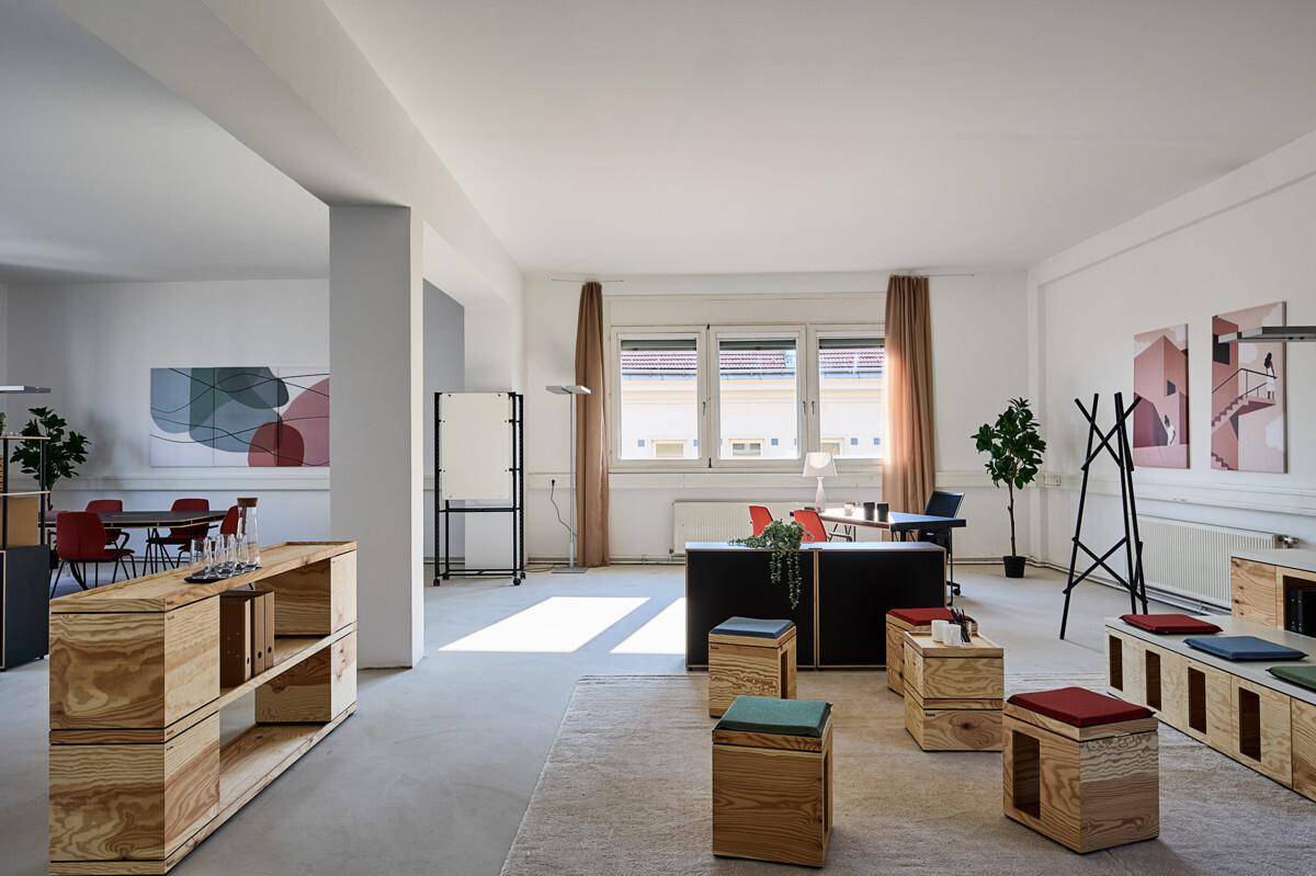 Heller, offener Büroraum mit modernen Holzmöbeln, weißen Wänden und großen Fenstern.