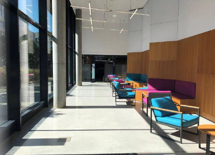 Helle, moderne Lobby mit großen Fenstern, farbenfrohen Sitzgelegenheiten und Holzakzenten, die zum Verweilen einlädt.