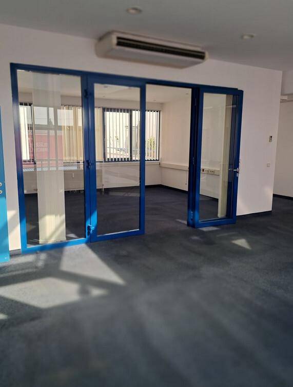 Heller Büroraum mit blauen Teppichboden, Glaswänden und einer Klimaanlage an der Decke.