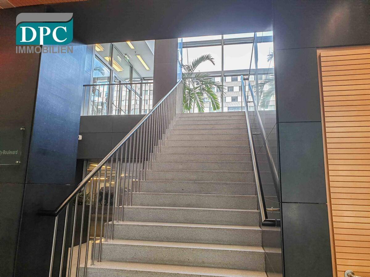 Elegante Treppe mit Edelstahlgeländer und großen Fenstern, die viel Licht hereinlassen und eine offene Gestaltung bieten.