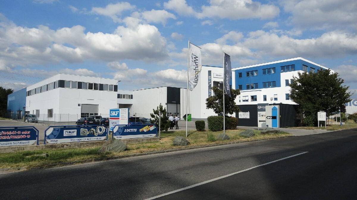 Weitläufiges Gewerbegebiet mit mehreren modernen Gebäuden, Straße und Beschilderung unter bewölktem Himmel.