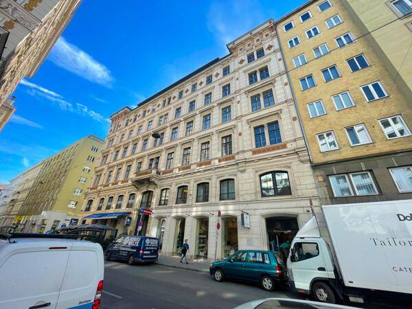 Historisches Gebäude an einer belebten Straße mit Geschäften und anderen Gebäuden unter blauem Himmel.