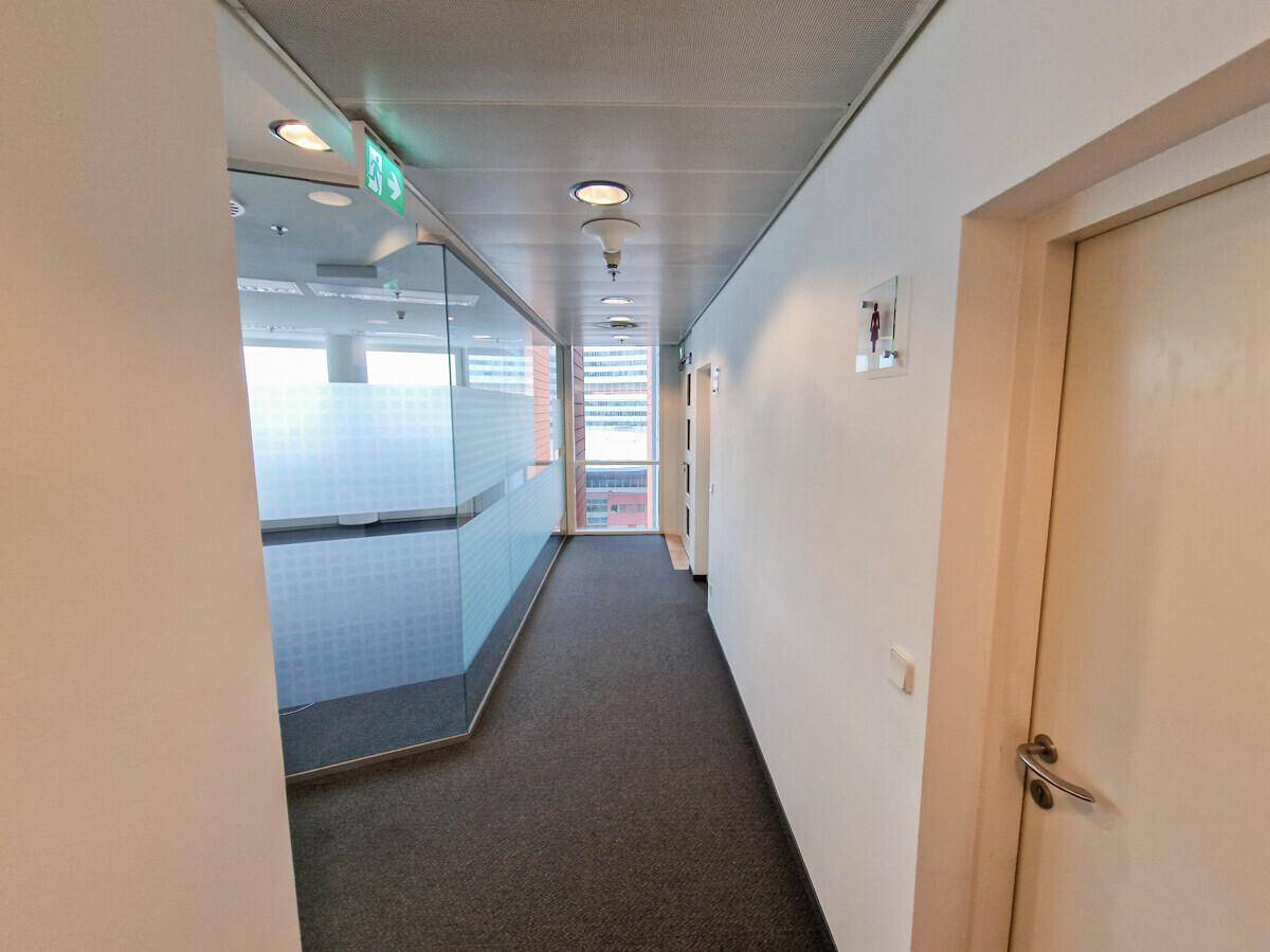 Büroflur mit Teppichboden, Glaswänden und Türen zu den Sanitäranlagen, die eine klare Orientierung bieten.