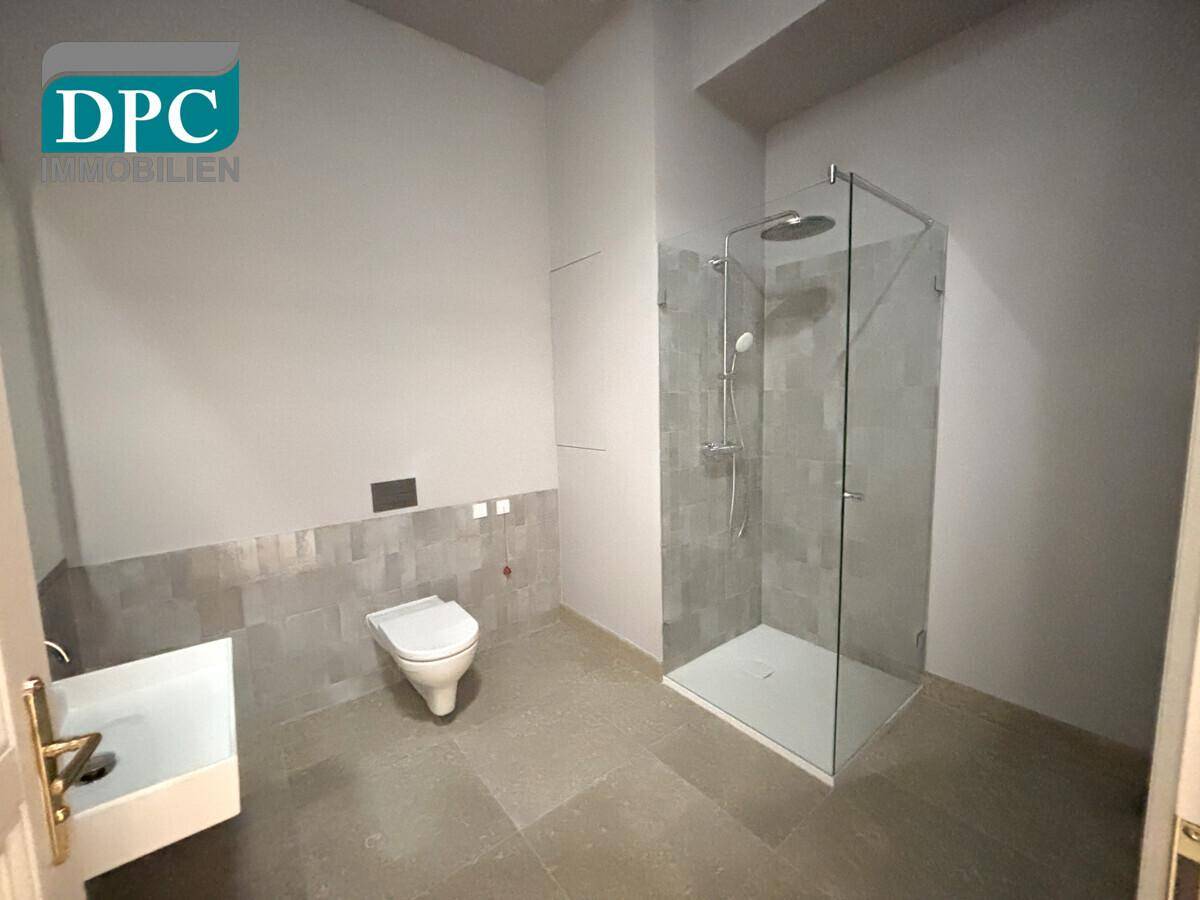 Modernes Badezimmer mit ebenerdiger Dusche und wandhängendem WC in neutralen Farbtönen.