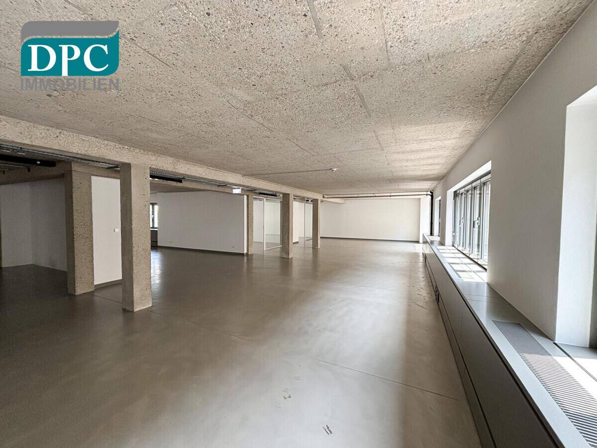 Heller, weitläufiger Bürobereich mit Sichtbetondecke, großen Fenstern und modernem Betonboden.