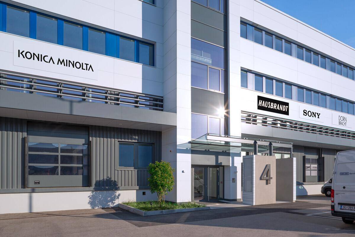 Moderner Eingangsbereich eines Bürogebäudes im Business Park mit Glasvordach und Firmenlogos.