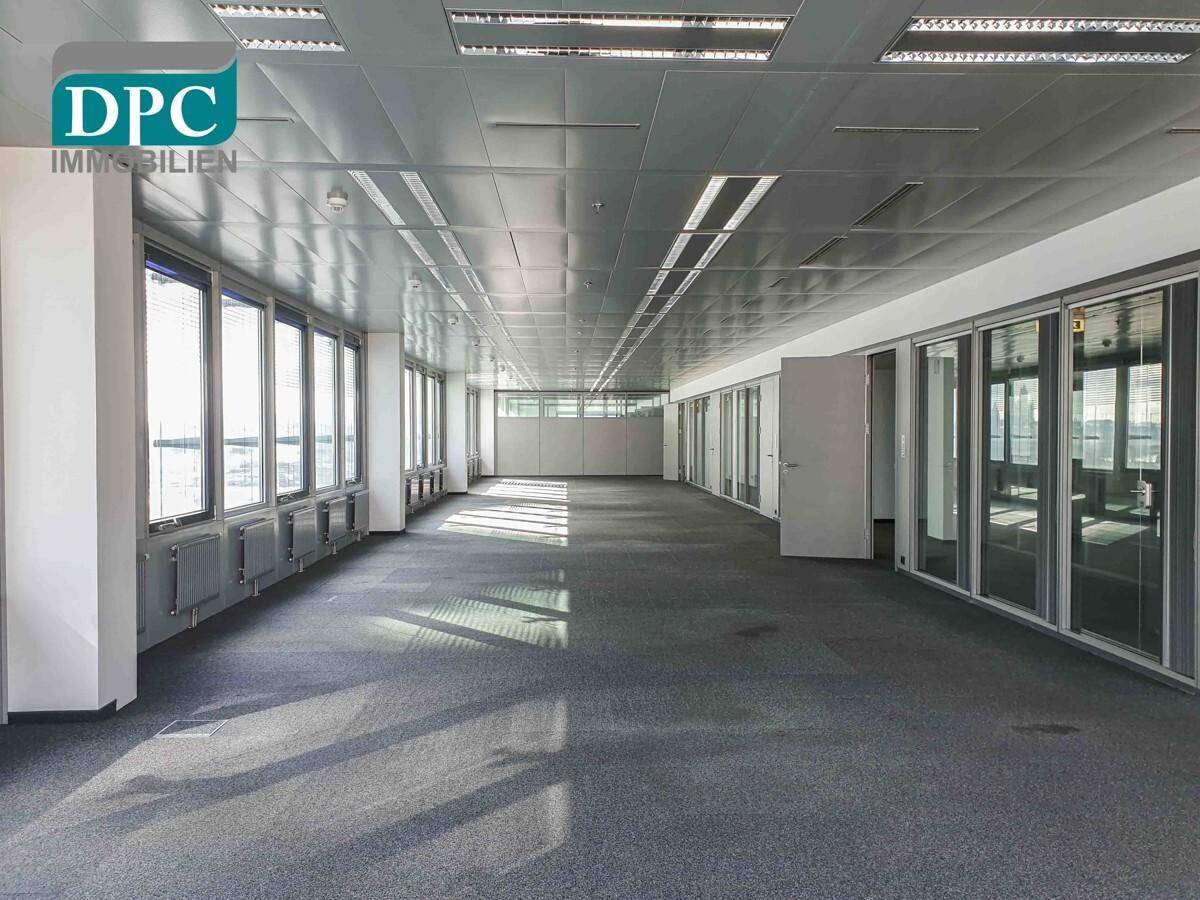 Weitläufiges Büro mit Teppichboden, vielen Fenstern und Glastrennwänden für separate Arbeitsbereiche, hell und modern.