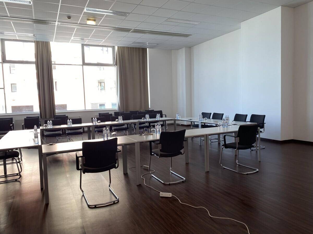 Großer Konferenzraum mit mehreren Tischen und Stühlen, bereit für Besprechungen oder Schulungen mit viel Tageslicht.
