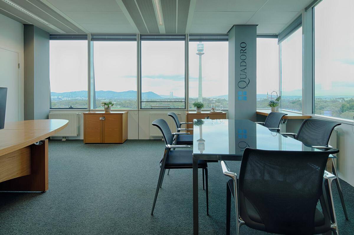 Modernes Büro mit Schreibtischen, Konferenztisch und großen Fenstern mit Blick auf die Stadt.