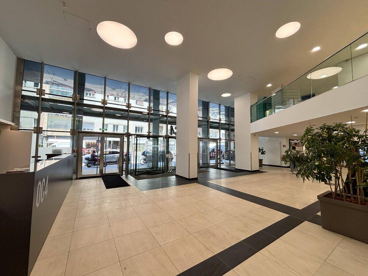 Moderne und helle Lobby mit hoher Decke, Glasfassade und Fliesenboden, einladender Empfangsbereich.