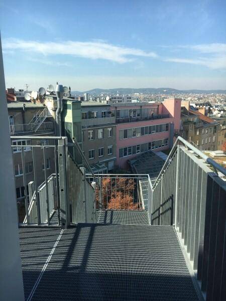 Metalltreppe im Freien mit Gitterrosten, die einen Blick auf die umliegende Stadtlandschaft und Gebäude freigibt.