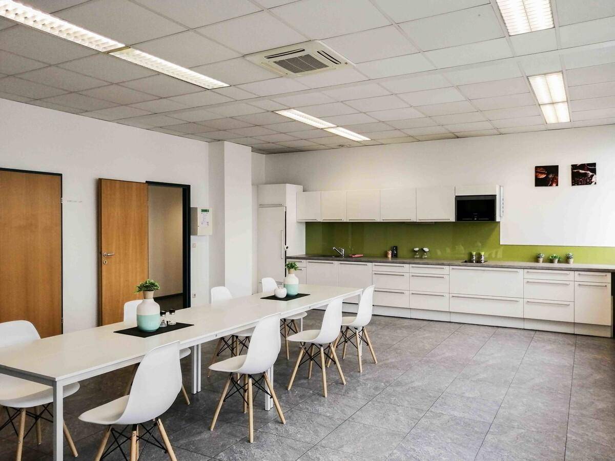 Geräumige Teeküche mit langer Tafel, weißen Schränken und grüner Rückwand.
