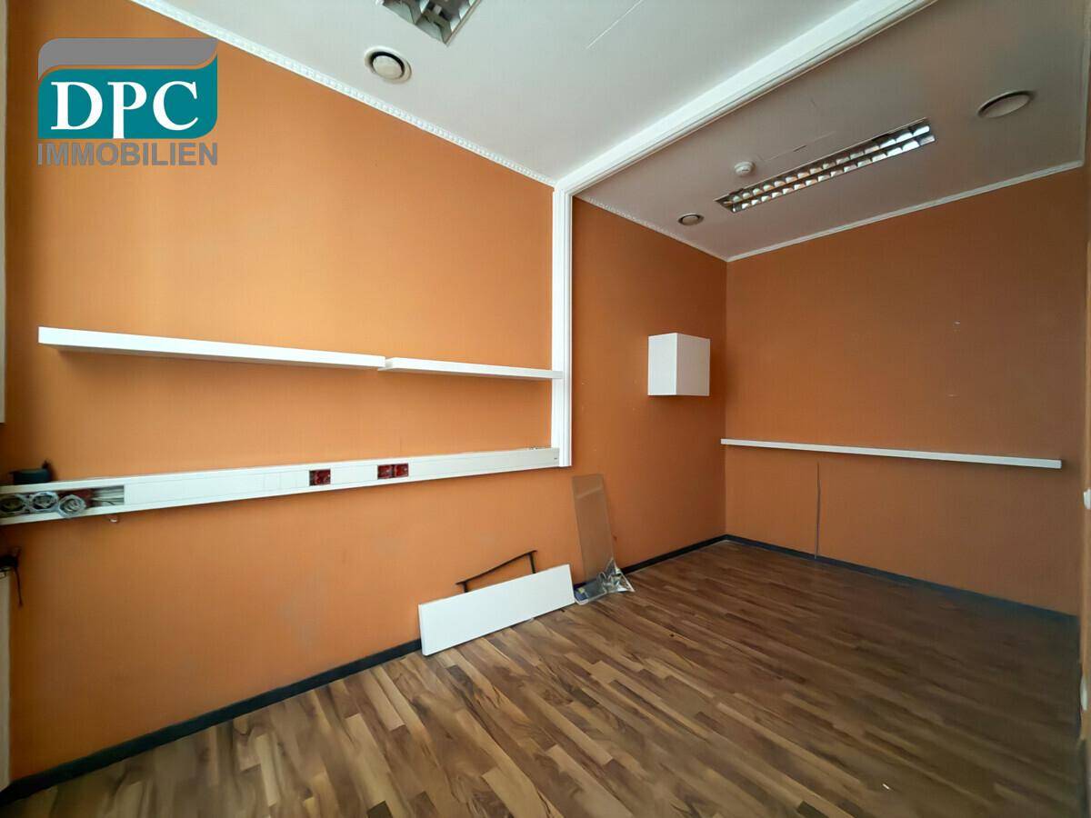 Kleiner Büroraum mit orangefarbenen Wänden, Holzboden und praktischen weißen Regalen.