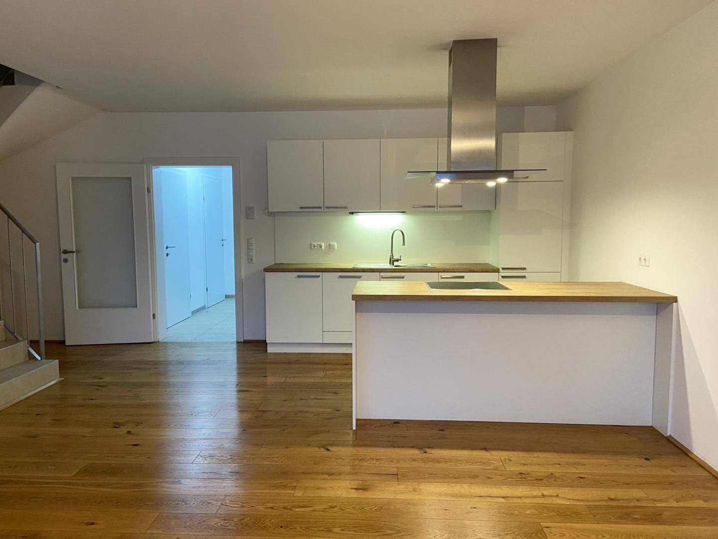 Moderne Einbauküche mit Kochinsel, Holzarbeitsplatte und Zugang zum Treppenhaus.