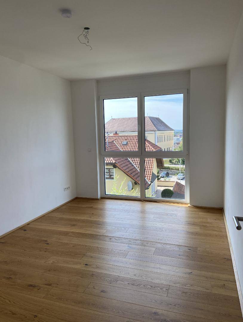 Lichtdurchflutetes Zimmer mit Parkettboden und großem Fenster mit Ausblick.