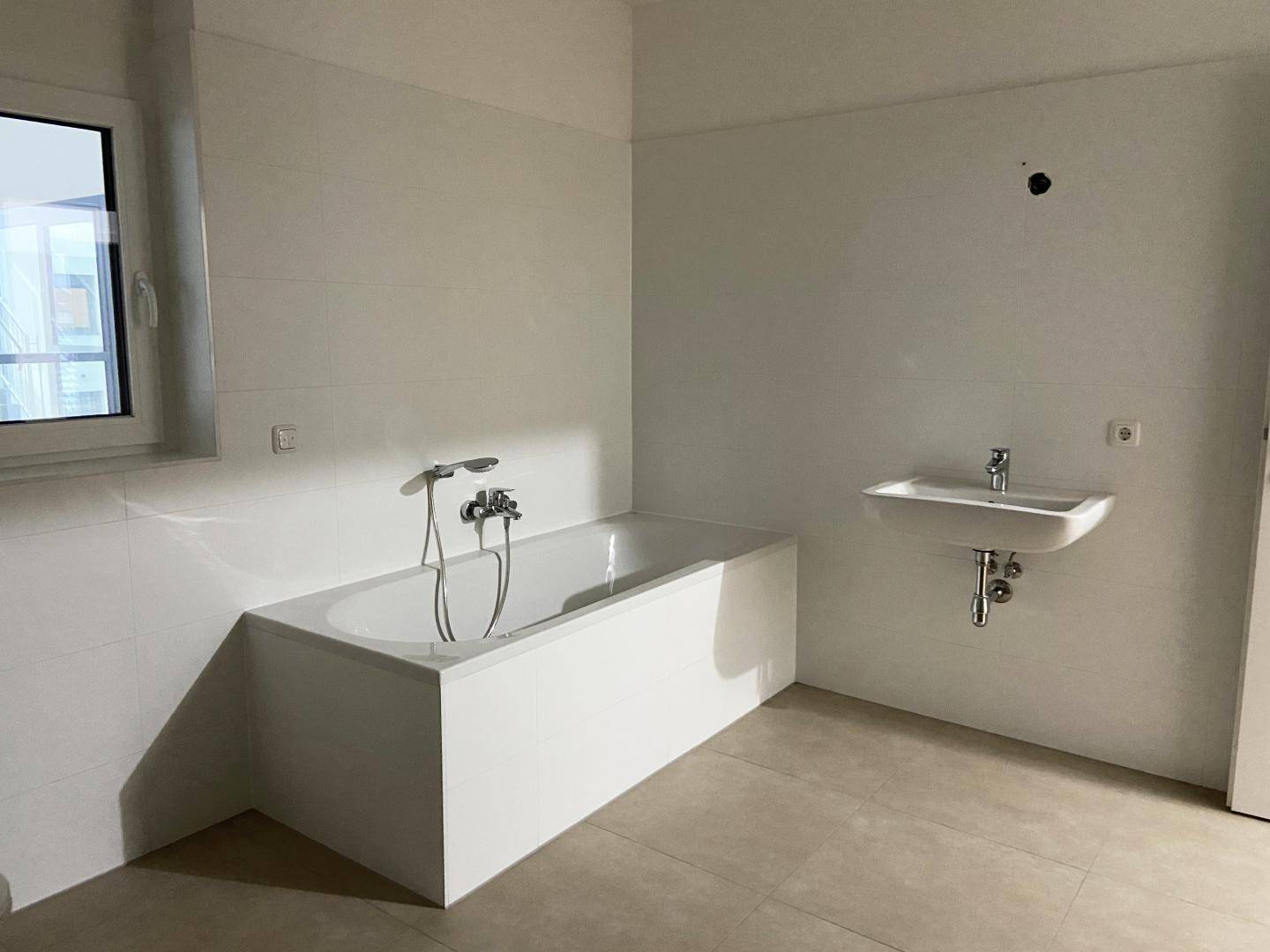 Modernes Badezimmer mit Badewanne, Waschbecken und Fenster für Tageslicht.