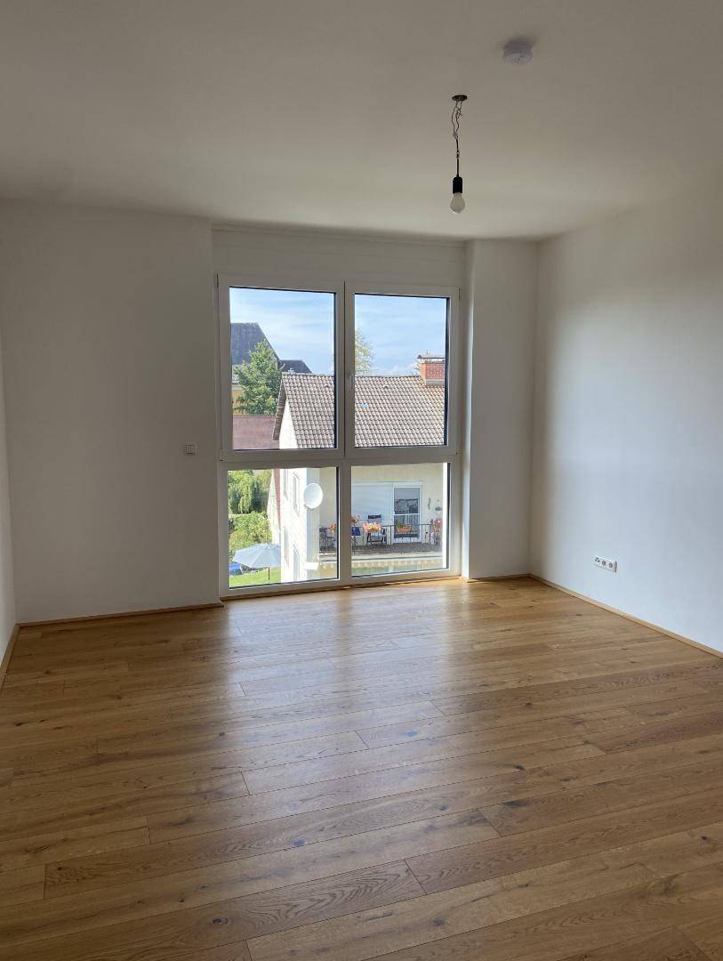 Helles Zimmer mit Parkettboden und großem Fenster mit Blick auf den Garten.