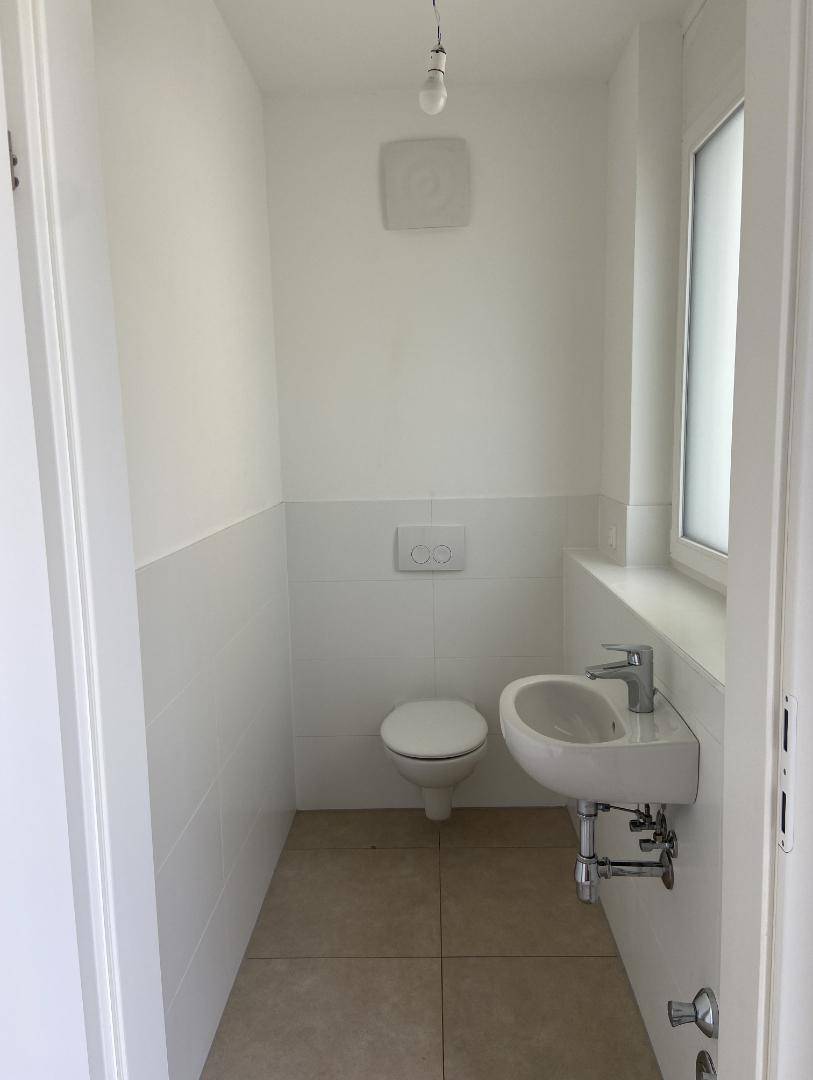 Modernes Gäste-WC mit wandhängendem WC, kleinem Waschbecken und Fenster.