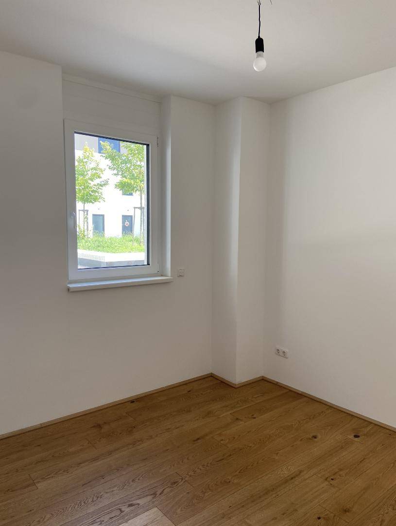 Helles Schlafzimmer mit Parkettboden und Fenster mit Blick ins Grüne.