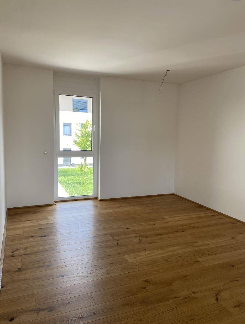 Helles Zimmer mit Parkettboden und Fenster mit Blick auf den Außenbereich.