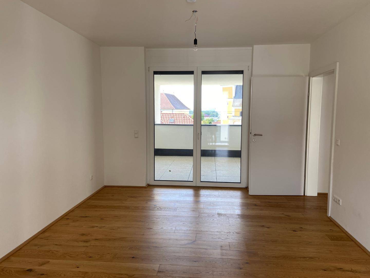 Helles Zimmer mit Parkettboden und großem Zugang zu einem Außenbereich.