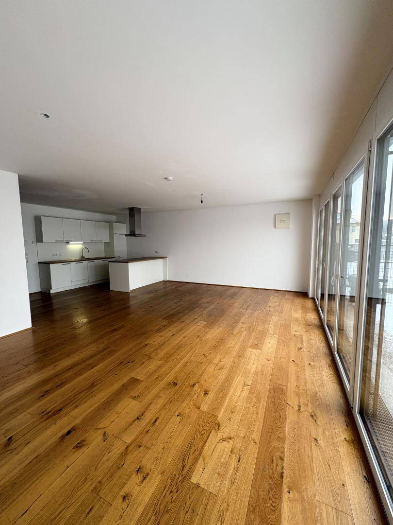 Geräumiger offener Wohn-Essbereich mit moderner Küche und großen Fenstern.