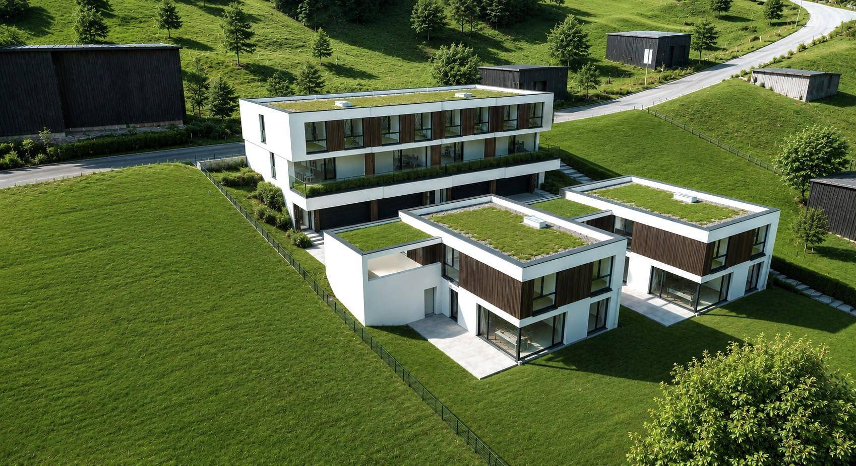 Moderne Wohngebäude mit begrünten Flachdächern, umgeben von grünen Hügeln und Bäumen.